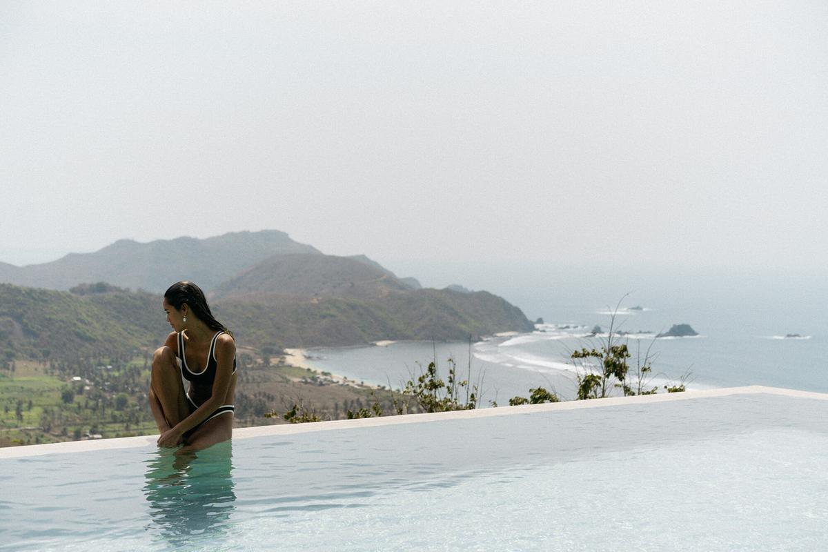 A guest sitting at the edge of an infinity pool above the bay